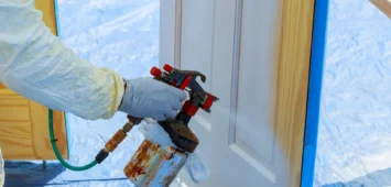 Worker with airbrush painting House repair paint the wooden door in white color with a spray